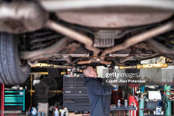 repairman - auto mechanic, caucasian white man with tattoos on hands, working in a car repair shop - fixing suspension of the car elevated on the lift. - tyre bridge stock pictures, royalty-free photos & images