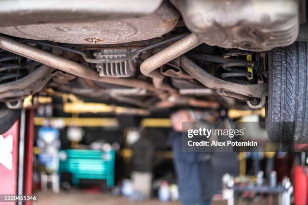 reparador - mecânico de automóveis, homem branco caucasiano com tatuagens nas mãos, trabalhando em uma oficina de reparação de carros - fixação de suspensão do carro elevado no elevador. concentre-se em primeiro plano, o homem está desfocado no pa - elevator bridge - fotografias e filmes do acervo