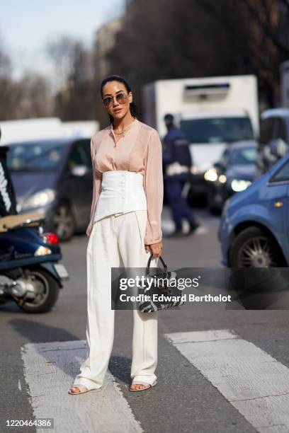 Tamara Kalinic wears sunglasses, a pink flowing shirt, a white corset, white flare pants, a Tod's balck and white zebra print bag, outside Tod's,...