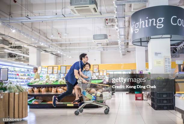 ein asiatisches chinesisches mädchen, das in einem einkaufswagen sitzt und von ihrem vater geschoben wird. sie haben spaß im supermarkt. - shopping cart stock-fotos und bilder