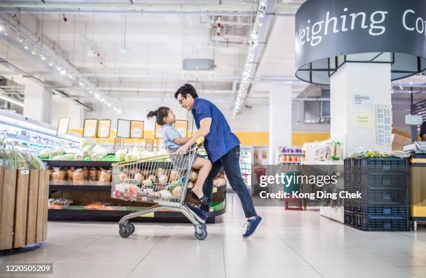 een aziatische chinese meisjeszitting in een boodschappenwagendie door haar vader wordt geduwd. ze hebben plezier in de supermarkt. - shopping trolleys stockfoto's en -beelden