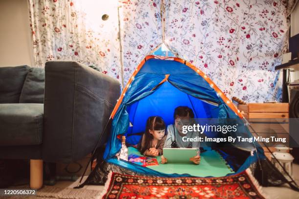 little sisters using digital tablet in a camping tent at home in the evening. - camping indoors stock pictures, royalty-free photos & images