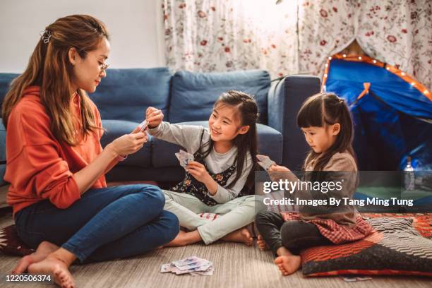 mom & daughters playing card games joyfully at home with a campfire & camping tent setting besides them in the evening.. - camping games stockfoto's en -beelden