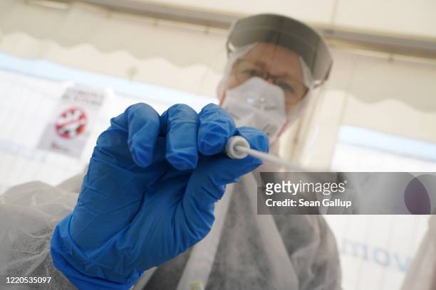 An employee of the Berlin-Mitte district health office wearing PPE protective gear demonstrates taking a throat swab sample during a press...