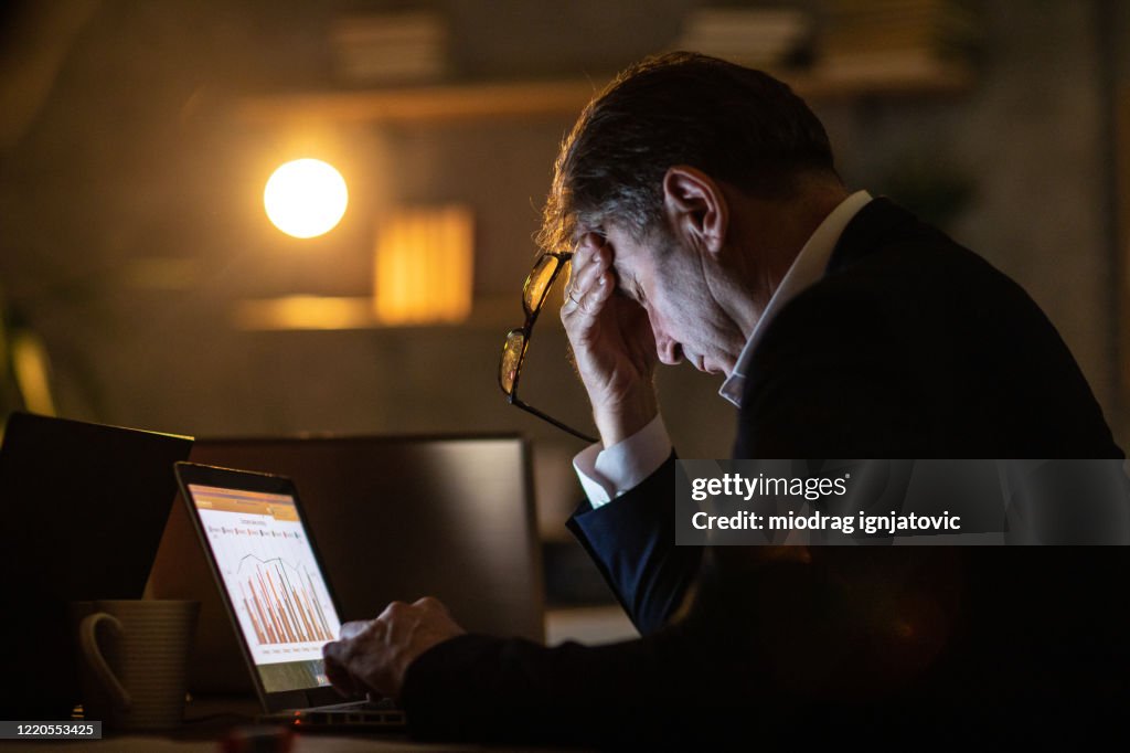 Vermoeide mens die laptop laat bij nacht in bureau gebruikt