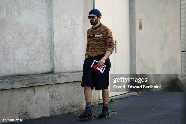 Guest wears a blue beanie hat, sunglasses, a Prada wool pullover, black shorts, socks, black leather shoes, outside Prada, during Milan Fashion Week...