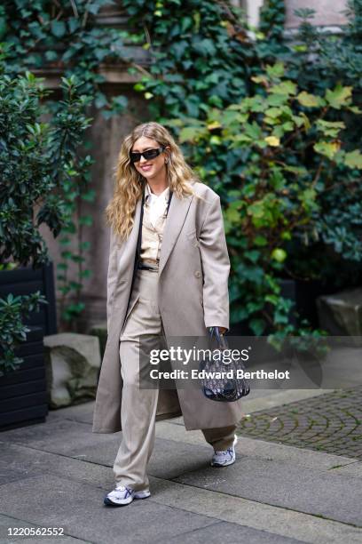 Emili Sindlev wears sunglasses, a gray long oversized coat, a Dior bag, a shirt, flare pants, sneakers, outside Koche x Pucci, during Milan Fashion...