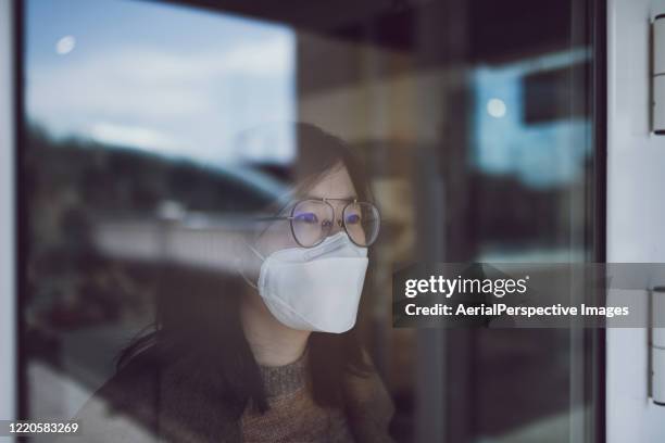 woman looking through window with mask - travel ban stock pictures, royalty-free photos & images