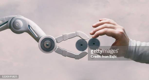 roboter und menschliche hand mit zahnrädern - menschlicher arm stock-fotos und bilder