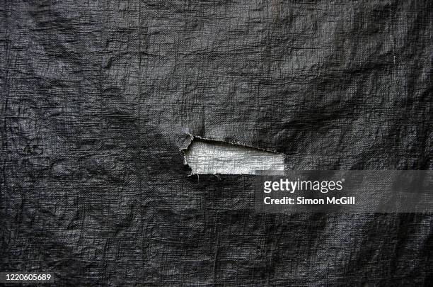 jagged rectangular tear in a black plastic tarp exposing a silver coloured tarp - tarpaulin 個照片及圖片檔
