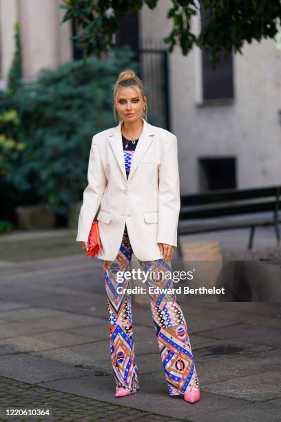 Guest wears a white oversize blazer jacket, colorful flare pants with printed patterns, a red clutch, pink pointy shoes, outside Koche x Pucci,...