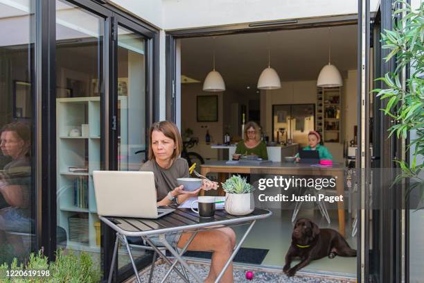 woman working from home. her family are eating lunch in the background - telecommuting eating stock pictures, royalty-free photos & images