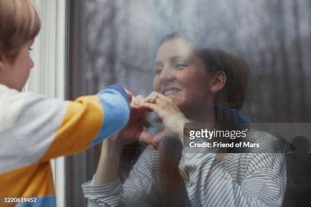young boy looks through window at mother who is in quarantine and social distancing - quarantäne stock-fotos und bilder