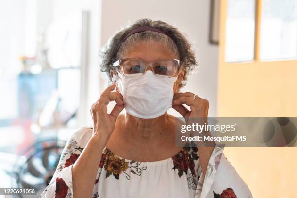 femme aîné mettant un masque protecteur sur son visage - face mask coronavirus photos et images de collection