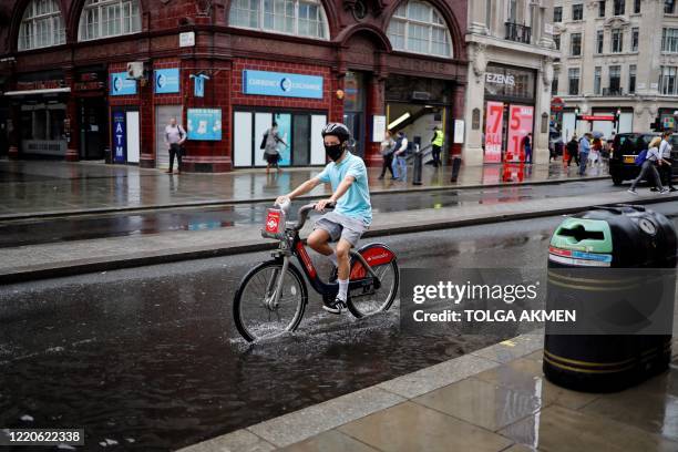 Person wearing PPE , of a face mask or covering as a precautionary measure against COVID-19, reacts as they cycle through a puddle as they are caught...