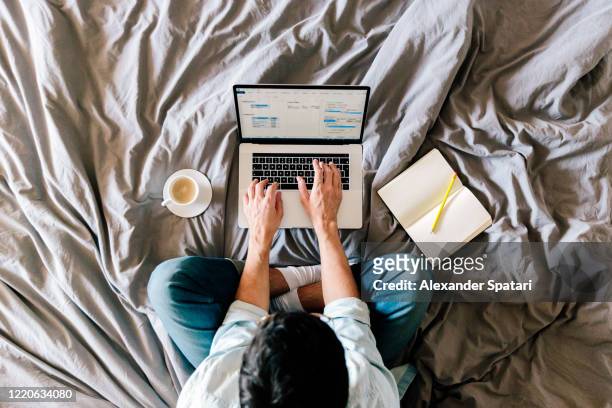 overhead view of a man working on a laptop from his bed at home - businessman working on a laptop with a coffee stock pictures, royalty-free photos & images