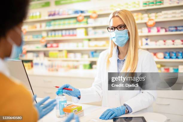 pharmacist with protection mask giving instructions on how to use medicine to a client. - pharmacy mask stock pictures, royalty-free photos & images