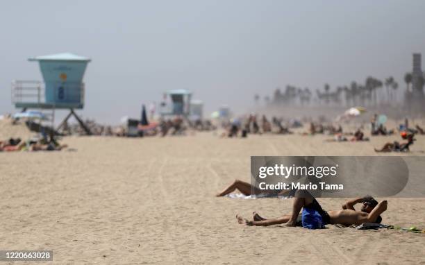 People gather on Huntington Beach which remains open amid the coronavirus pandemic on April 23, 2020 in Huntington Beach, California. Neighboring...