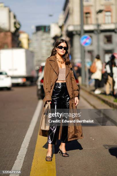 Paola Alberdi wears sunglasse,s a chain necklace, a brown long coat, a gray crop top, black shiny pants, a brown bag, mesh shoes, outside Max Mara,...