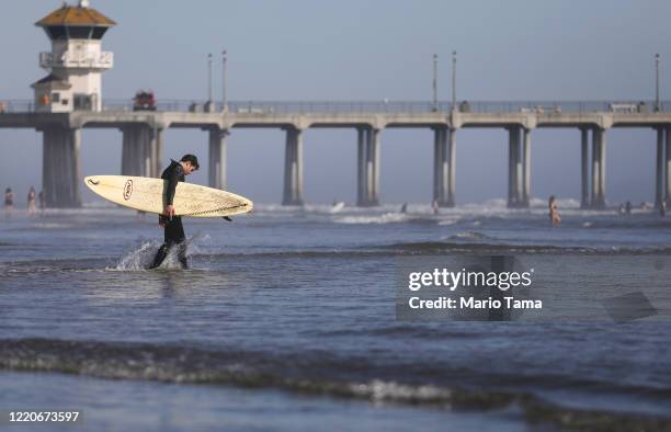 Surfer enters the water on Huntington Beach which remains open amid the coronavirus pandemic on April 23, 2020 in Huntington Beach, California....