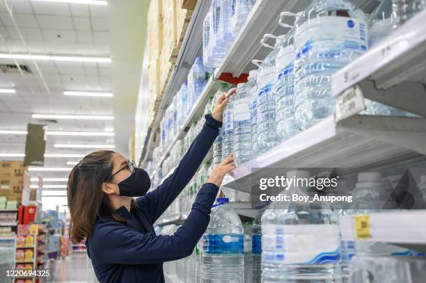 portrait of asian woman wearing mask for protect herself from virus disease while shopping bottle water in supermarket for stocking up supplies during covid-19 pandimic outbreak. - gallon stock-fotos und bilder