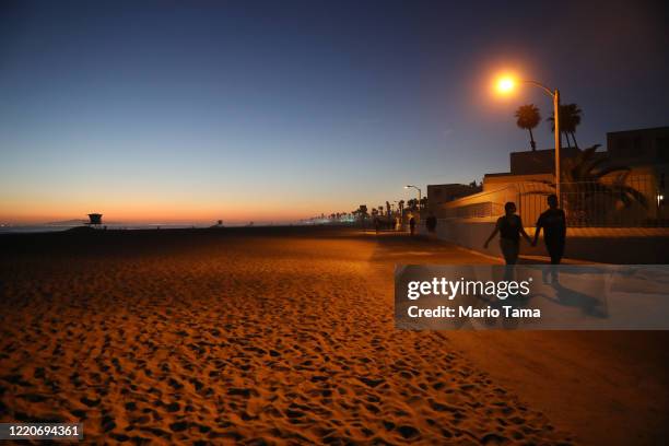 People walk at dusk on Huntington Beach, which remains open amid the coronavirus pandemic, on April 23, 2020 in Huntington Beach, California....