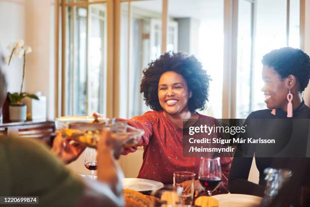 smiling woman passing food to friend at table - thanksgiving day stock pictures, royalty-free photos & images