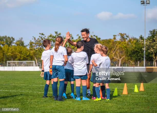 lächelnder coach high-fiving young footballers at practice - coaching stock-fotos und bilder