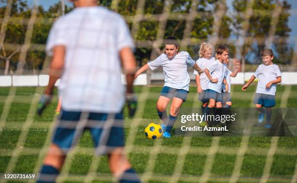 young boy footballer practicing goal kick with teammates - boy goalie standing in front of goal net stock pictures, royalty-free photos & images