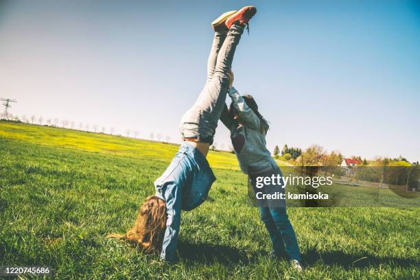 ragazze felici che giocano sul prato estivo - cercando il cavalletto - fare la verticale sulle mani foto e immagini stock