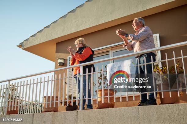 senior couple on their 70s clapping hands at balcony with a hand drawn rainbow fix at bannister - nhs rainbow stock pictures, royalty-free photos & images