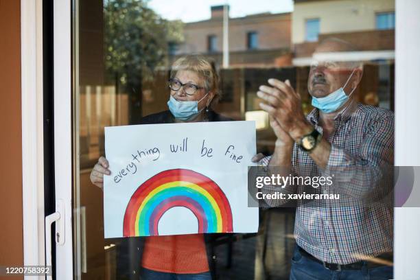 senior couple on their 70s clapping hands at showing a hand drawn rainbow at home in quarantine - clapping hands covid stock pictures, royalty-free photos & images