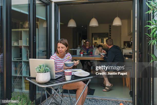 women working from home. bowl of pasta in hand. her family eat in the background - dog eats out girl photos et images de collection