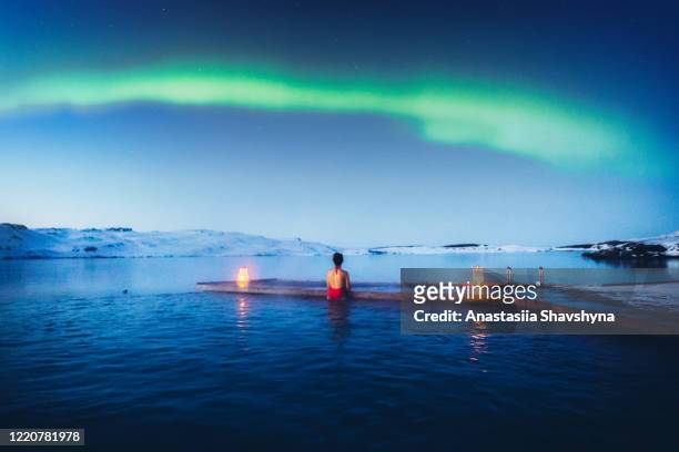 junge frau genießt die malerische aussicht auf die nordlichter über dem see und pool in island - iceland stock-fotos und bilder