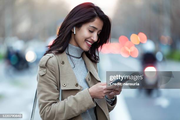 Pretty young woman listening to music with wireless earphones and the smartphone in the street.