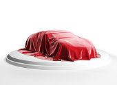 Car covered with red silk cloth on a white podium. Isolated with clipping path.