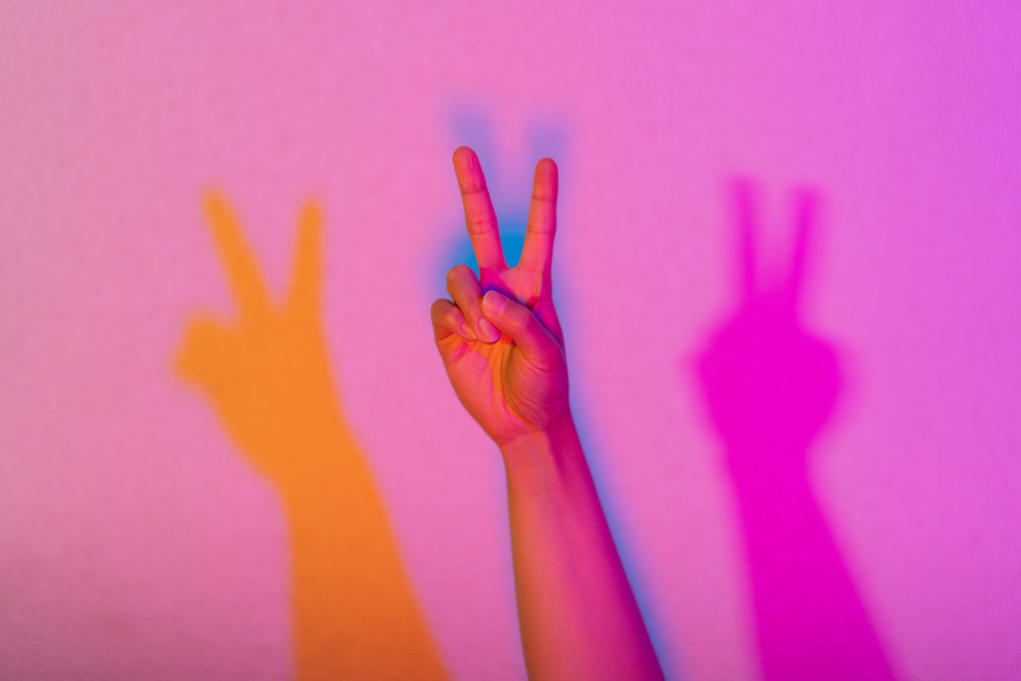 Close-up photo of hand lit by neon lights doing peace sign Close-up photo of hand lit by neon lights doing peace sign