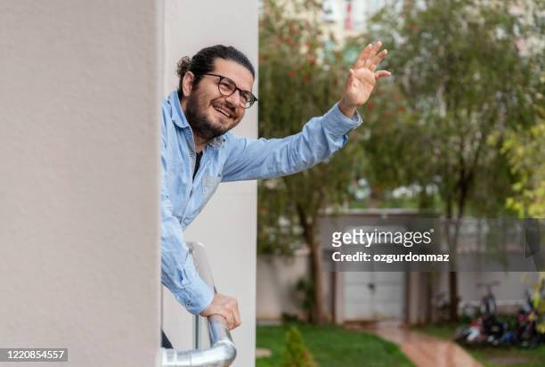 positive man staying on the balcony and greeting the neighbors during covid-19 pandemic - neighbour stock pictures, royalty-free photos & images