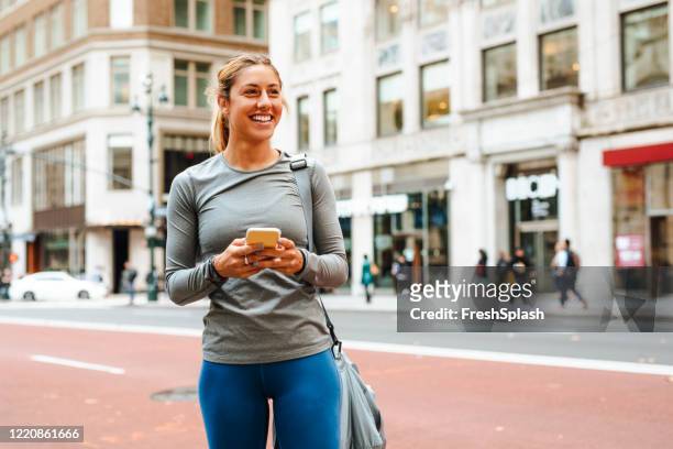 athletic blonde woman taking a moment to check her phone on her way to the workout - tights stock pictures, royalty-free photos & images