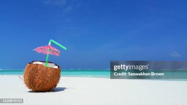 fresh coconut juice on white sand with blue water and clear blue sky in the background - close-up shot - noix de coco photos et images de collection