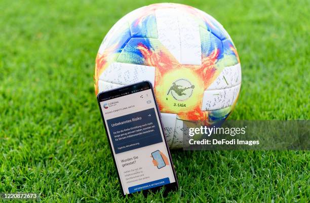 Smartphone is leaning against a play ball with the open Corona Warn app on the screen prior to the 3. Liga match between FC Viktoria Koeln and TSV...