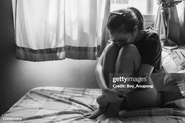 portrait of depressed/stressed woman sitting alone on the bed in the bedroom, monochrome tone. - abuse fotografías e imágenes de stock