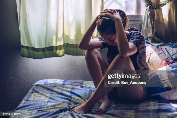 portrait of depressed/stressed woman sitting alone on the bed in the bedroom. - distraught photos et images de collection