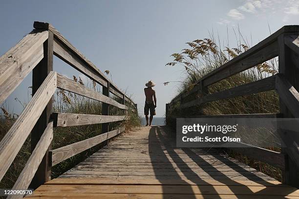 Surfer checks out the waves on a nearly empty beach along North Carolina's Outer Banks August 25, 2011 in Nags Head, North Carolina. Dare County,...