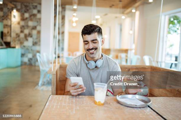 en millennial latino man äter mellanmål och använder telefon för meddelanden och e-banking - modern manlighet bildbanksfoton och bilder