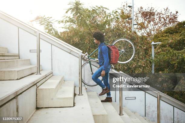 mid adult commuter with backpack carrying bicycle up stairs - side view carrying stock pictures, royalty-free photos & images