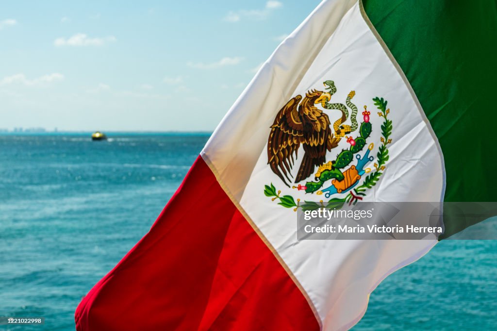 Real Mexican flying flag against sea background and blue sky