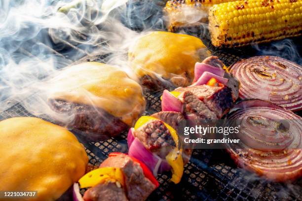lean gezonde cheeseburgers, kebobs, ui plakjes en oren van maïs op een houtskoolgrill - burger grill stockfoto's en -beelden