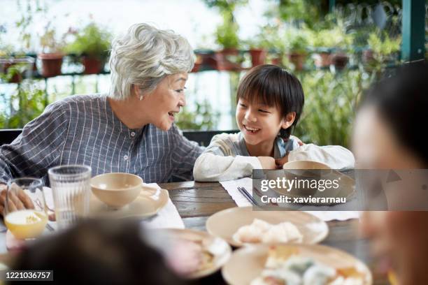 young chinese boy laughing with grandmother at family meal - hong kong grandmother stock pictures, royalty-free photos & images