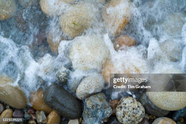 Pebbles in pastel shades of colour as wave soaks them on the seashore on Isle of Arran, Scotland.